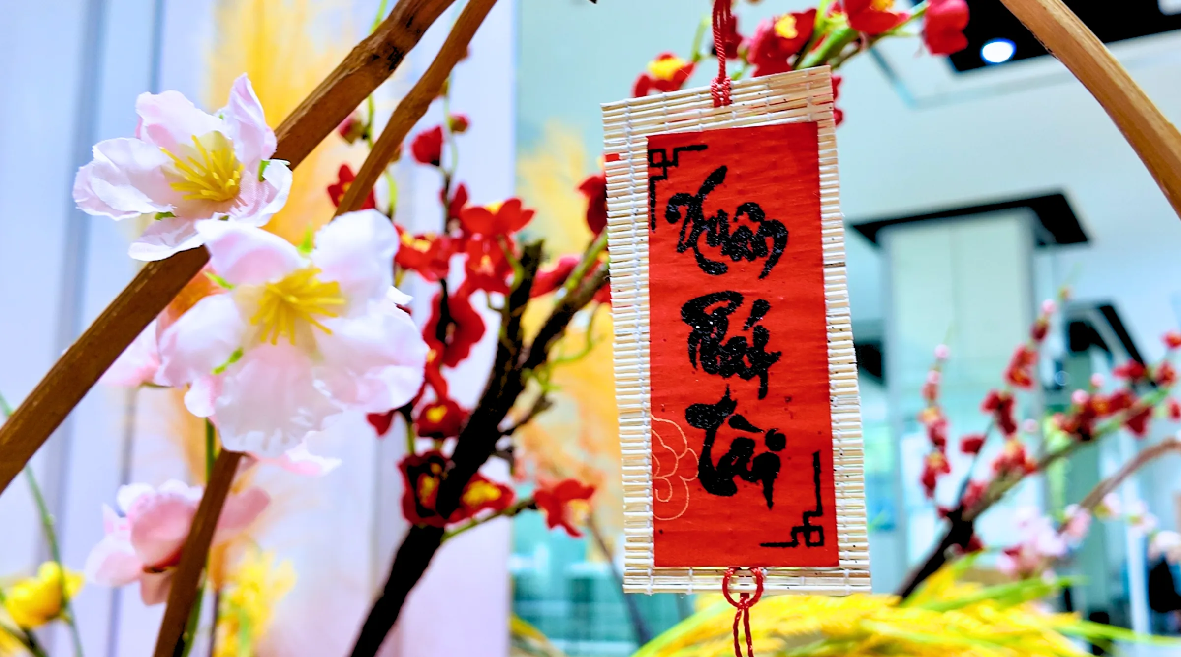 Chi tiết câu chúc xuân treo trên cành đào tạo điểm nhấn cho không gian trang trí Tết tại trường